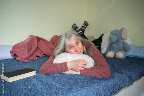 Senior woman lying on bed hugging pillow showing emotional comfort