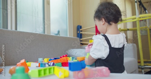 Toddler builds with colorful plastic blocks on a gray sofa in a brightly lit home environment, focusing on early childhood development, creative learning, and safe domestic play.