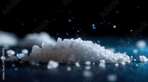 A close-up view of crystalline salt or chemical substance, with particles in mid-air against a dark background, highlighting texture and light reflections