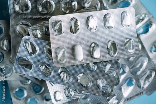 Fotografie Single white tablet remains in silver blister pack among empty medication wrappers
