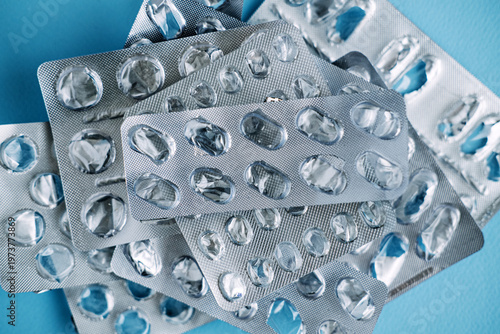 Collection of used medication blister packs lies scattered on blue surface. Non-recyclable medical waste, plastic pollution in healthcare, eco-friendly pharmacy trends.