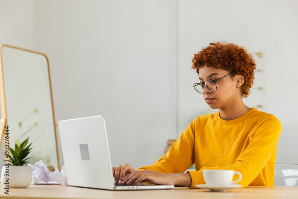 Fototapeta premium African american girl using laptop at home office looking at screen typing chatting reading writing email. Young woman having virtual meeting online chat video call conference. Work learning from home