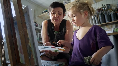 Child painting with an grandmother in a cozy art studio. Candid indoor moment of creativity and learning. Artistic lifestyle scene with real people and natural light.