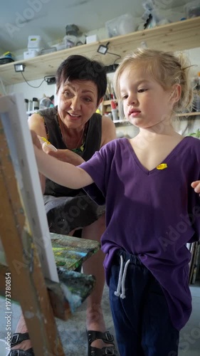 Child painting with an grandmother in a cozy art studio. Candid indoor moment of creativity and learning. Artistic lifestyle scene with real people and natural light.
