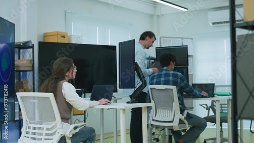 professional woman with glasses in modern AI development office focuses intently on coding at laptop while viewing large blue AI Assistant screen with glowing neural brain graphic, symbolizing machine