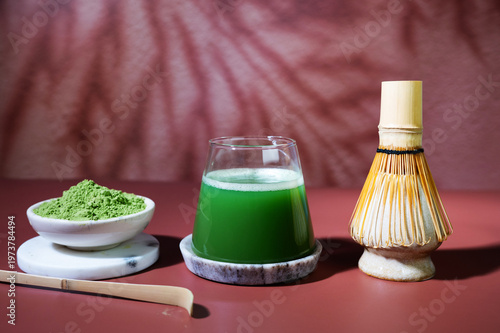 Close-up of matcha drink with foam in a glass, styled with traditional bamboo spoon and whisk.