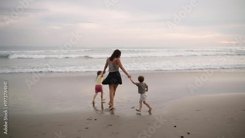 Mother, daughter, and son having fun together on the beach at sunset, enjoying quality family time by the ocean. Warm pink light, joyful atmosphere, and carefree moments of vacation, childhood