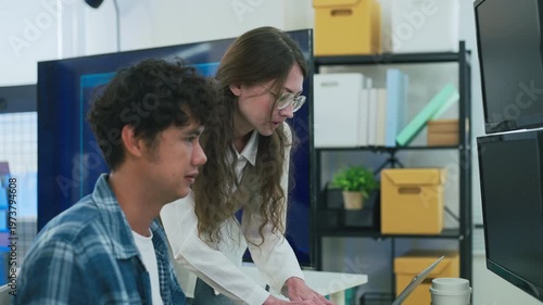 collaborative AI development team in modern tech office: young male developer coding on laptop while senior colleague leans over discussing code and data visualizations on multiple monitors	