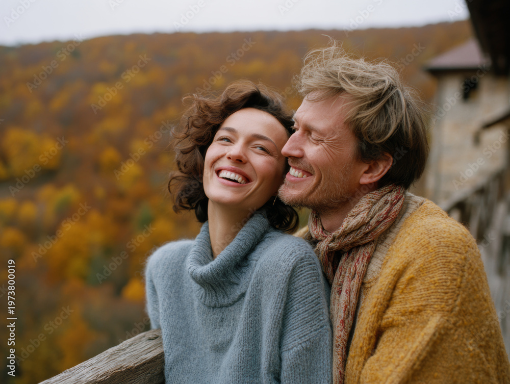 Fototapeta premium A happy couple wearing warm sweaters relaxes at their countryside retreat, taking in the stunning view of yellow and red autumn leaves. Peaceful, loving lifestyle.