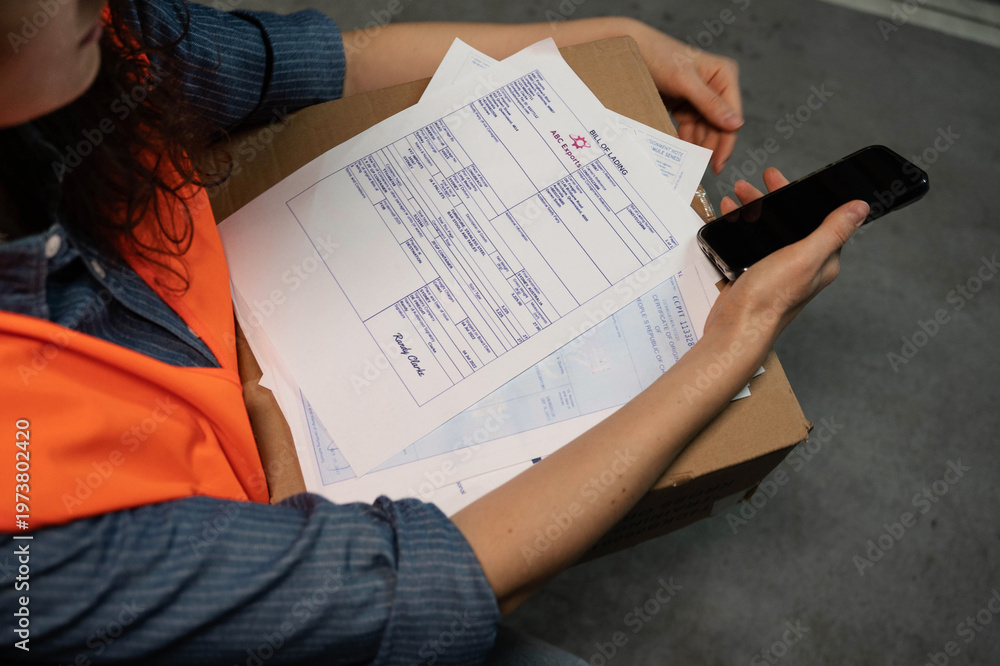 Naklejka premium A logistics company employee checks documents using a smartphone