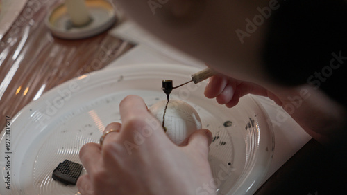 Close-up of hands painting a traditional Ukrainian Easter egg (Pysanka) with beeswax using a stylus (pysachok), preserving ancient folk traditions and symbols.