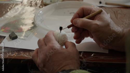 Close-up of hands painting a traditional Ukrainian Easter egg (Pysanka) with beeswax using a stylus (pysachok), preserving ancient folk traditions and symbols.