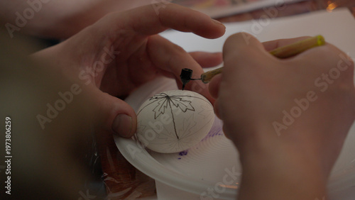 Close-up of hands painting a traditional Ukrainian Easter egg (Pysanka) with beeswax using a stylus (pysachok), preserving ancient folk traditions and symbols.