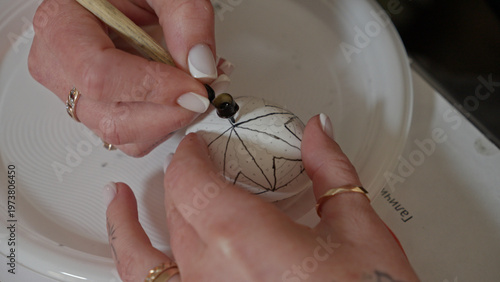 Close-up of hands painting a traditional Ukrainian Easter egg (Pysanka) with beeswax using a stylus (pysachok), preserving ancient folk traditions and symbols.