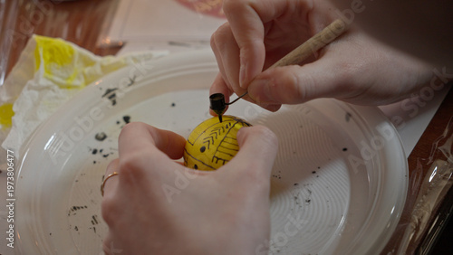Close-up of hands painting a traditional Ukrainian Easter egg (Pysanka) with beeswax using a stylus (pysachok), preserving ancient folk traditions and symbols.