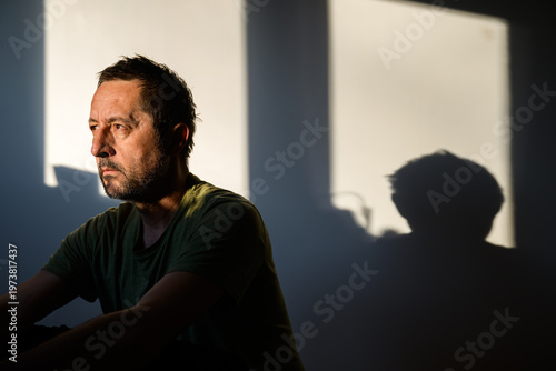 Close-up of thoughtful adult male in side light with glowing outline and moody shadows, expressive portrait conveying contemplation and inner strength.