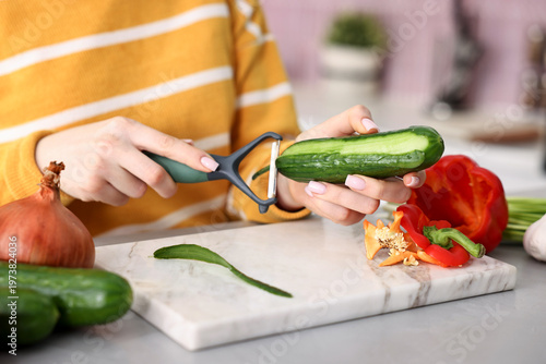 Tableau sur toile Woman peeling fresh cucumber at grey table with vegetables indoors, closeup
