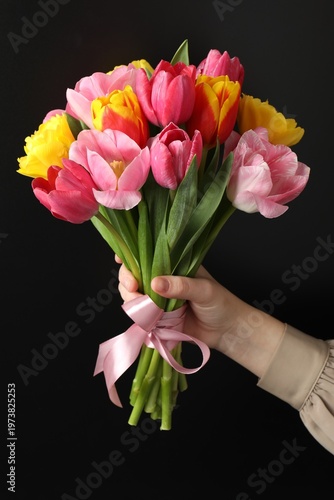 Woman with bouquet of aromatic bright tulips on black background, closeup. Beautiful greeting card