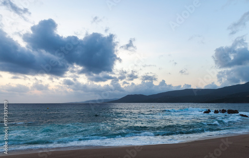 Dramatic view of shoreline with rocks in water, gently lapping waves, and a s...