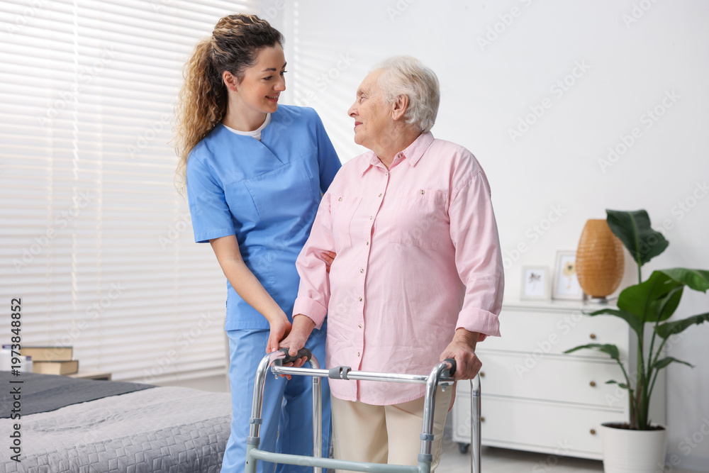 Fototapeta premium Care worker helping senior woman with walker indoors