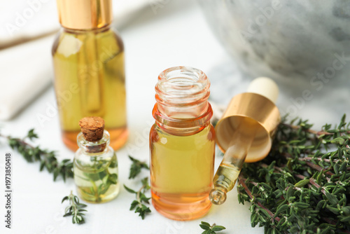 Thyme essential oil and fresh herbs on white table, closeup