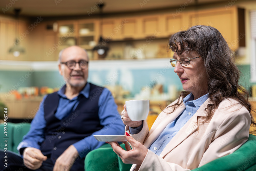 Fototapeta premium Retired senior couple, relaxing together, coffee in living room, peaceful home, retirement lifestyle. Husband and wife, comfort and companionship, longevity, independence, and domestic life.