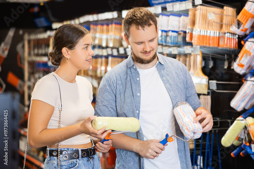 Married couple choose paint brush and paint roller together for their home renovation at a hardware store