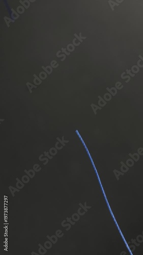 Metal scissors cutting blue thread on dark background