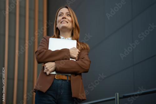 Konstfotografi Woman smiling looking up holding laptop outdoors