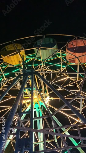 Close-up shot of a colorful Ferris wheel at night with vibrant green, yellow, and orange lights against a dark background