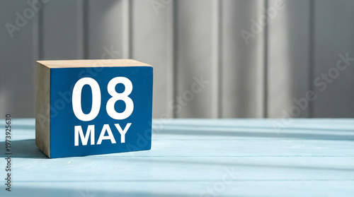 Wooden block calendar showing May 8th on a light blue table with a blurred background