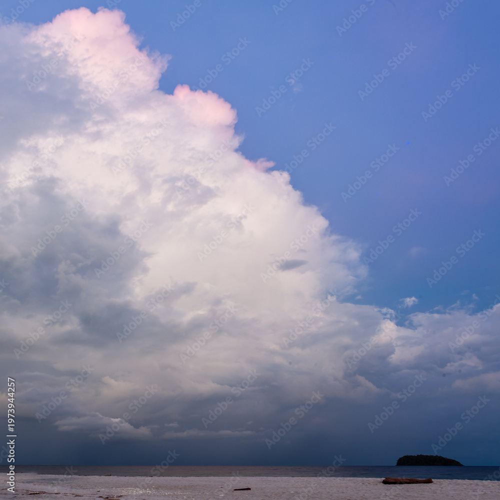 Obraz premium Koh Adang. Tarutao National Marine Park island silhouette. Calm Andaman Sea beneath towering storm cloud. Pink rim lighting on cloud.
