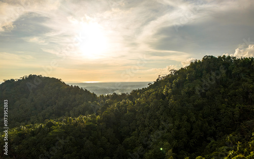 Majestic sunset paints the sky over lush green mountains in a tranquil natural paradise