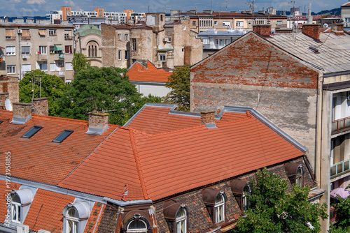 Fotografie View over dense city rooftops with red tile roofs, chimneys and weathered apartm