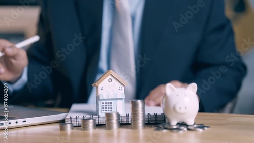 Businessman pointing at laptop and signing mortgage loan papers with focus on house model.