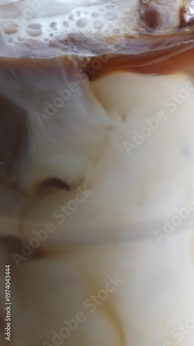 4K Vertical video Iced coffee with milk pouring into glass creating smooth swirl with ice cubes Refreshing cold beverage,Concept with rich texture ideal for cafe summer drink and commercial advertisin