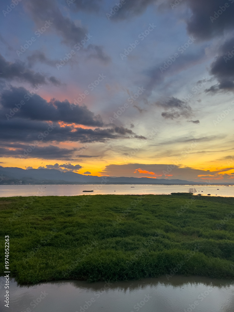 Obraz premium Sunset Over Water With Green Grass