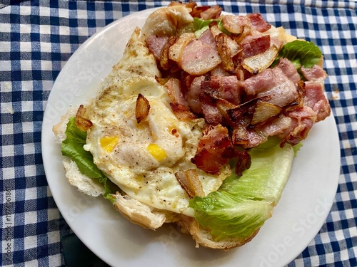 Homecooked fried egg and grilled bacon with fresh lettuce on a buttered coney roll for a mid-morning snack