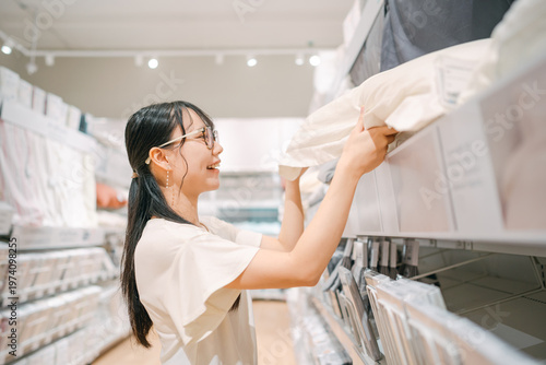 Obraz na plátně Smiling asian woman shopping choosing bed pillow product for home at indoors jap