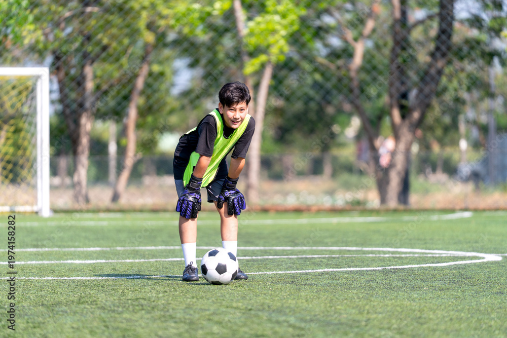 Obraz premium A boy stand and bend the body look like feel tired during practice of soccer ball in the field.