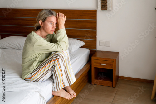 Sad alone middle aged woman sitting on bed