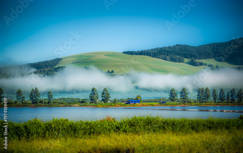 Green mountains contrast with the blue sky and a light mist.