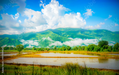 Green mountains contrast with the blue sky and a light mist.