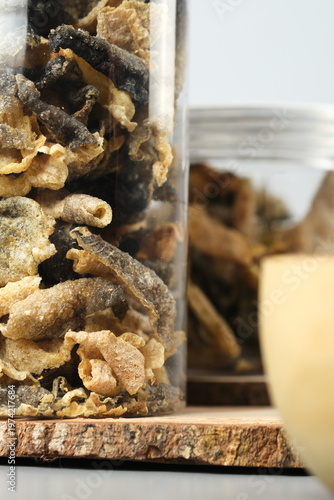 Clear jars with crispy fried salmon fish skins on rustic wooden surface. Perfect for food blogs, snack product packaging, culinary websites.