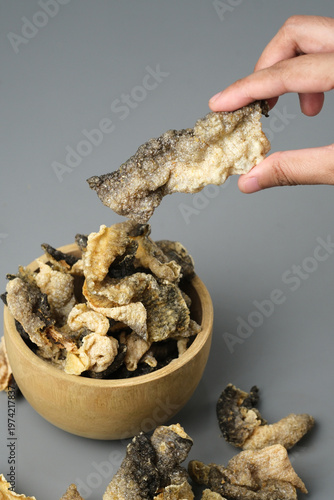 Person holds fried salmon fish skin over a bowl. Suitable for seafood lovers, food bloggers, restaurant menus, and cooking related designs.