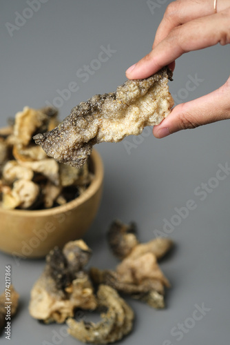Person holds fried salmon fish skin over a bowl. Suitable for seafood lovers, food bloggers, restaurant menus, and cooking related designs.