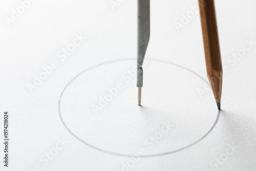 Drafting compass drawing circle on white paper background macro.