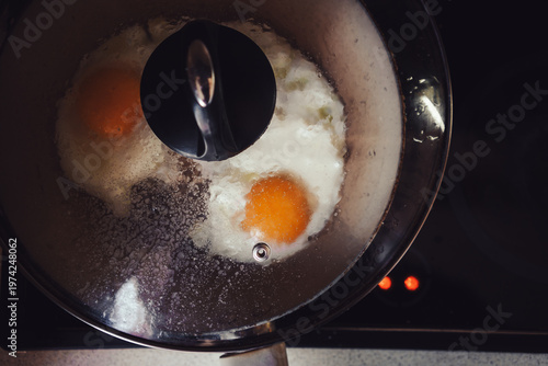 Two fried eggs in a pan under a glass lid