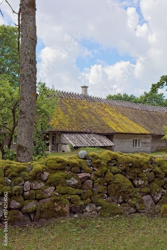 Traditional thatched-roof farmhouse and mossy stone wall  in summer, Koguva village, Muhu, Estonia, Europe.