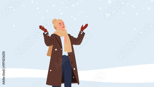 Joyful woman in a warm winter coat and scarf stands in a snowy field with her arms open to catch falling snowflakes.